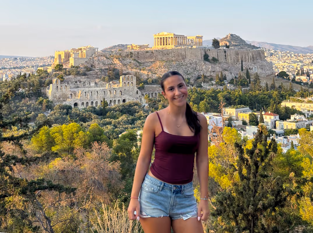 Guest at the Philopappos Hill viewpoint at golden hour, the Acropolis and the Odeon of Herodes Atticus across the valley behind her