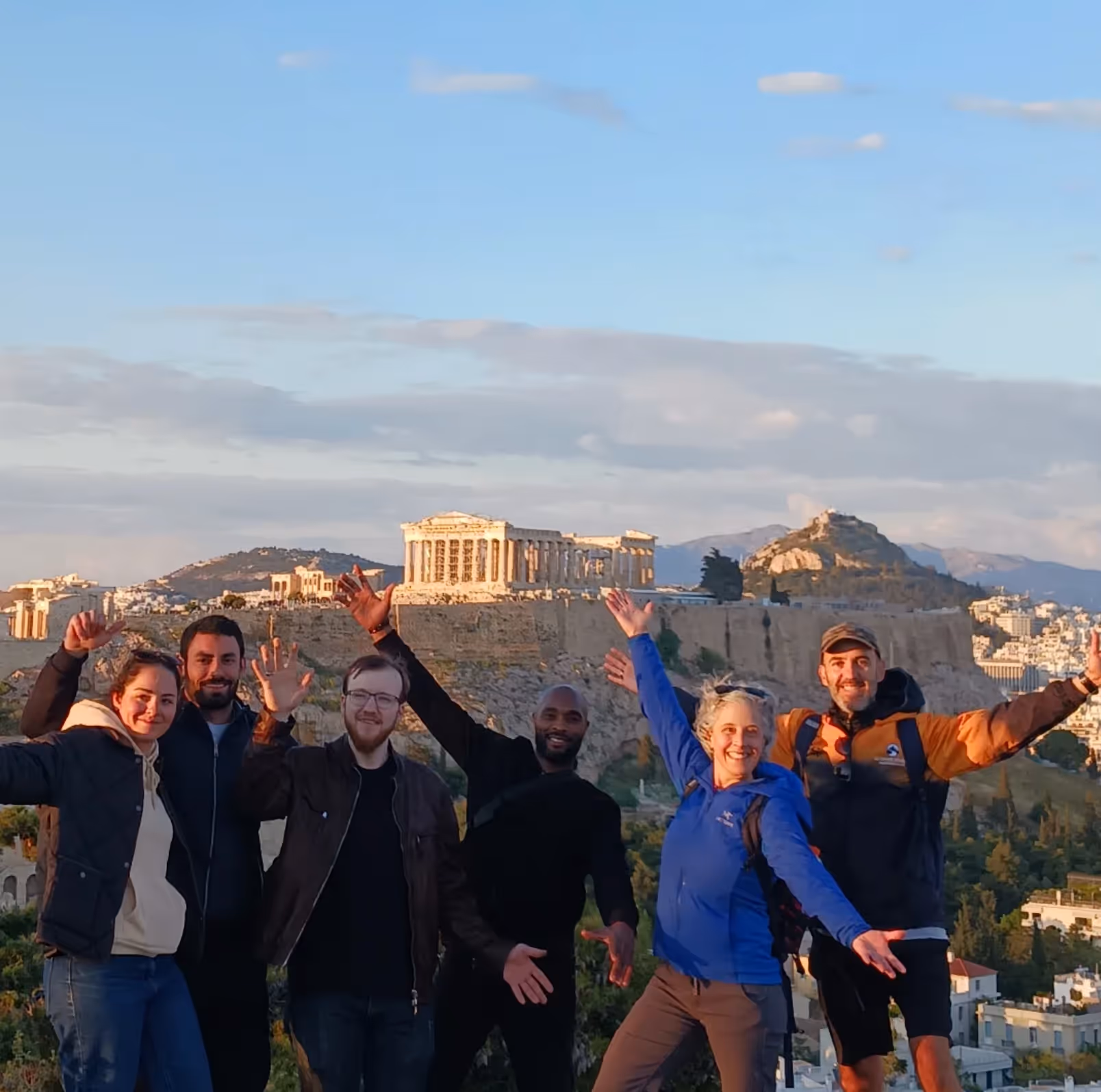 Hikers celebrating at the summit, the Acropolis and Lycabettus Hill behind them in the morning light
