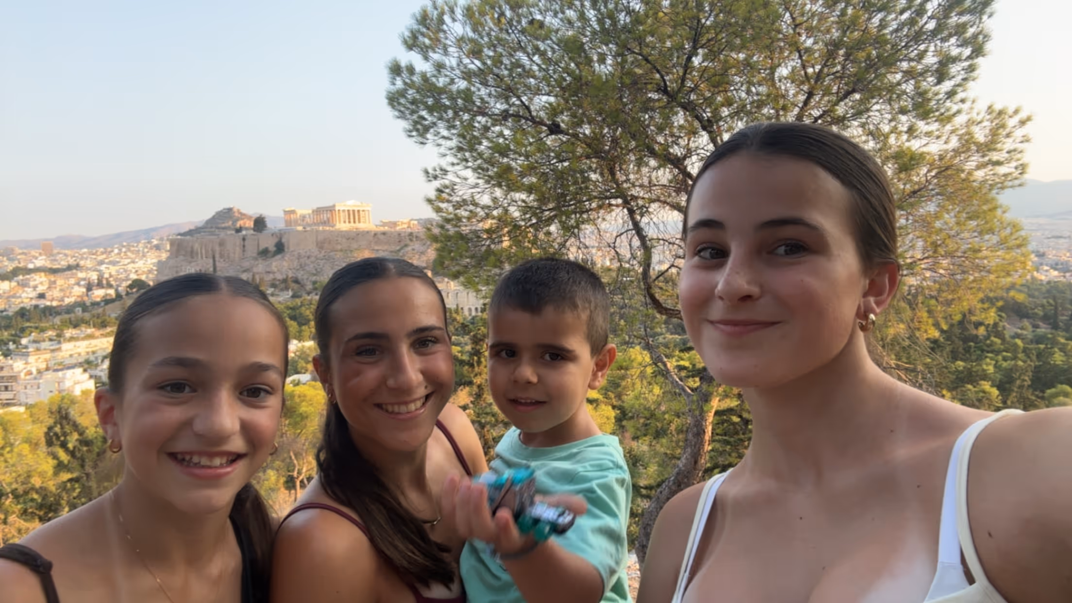 Four guests at the Philopappos Hill viewpoint at sunset, the Parthenon and the Acropolis lit up behind them
